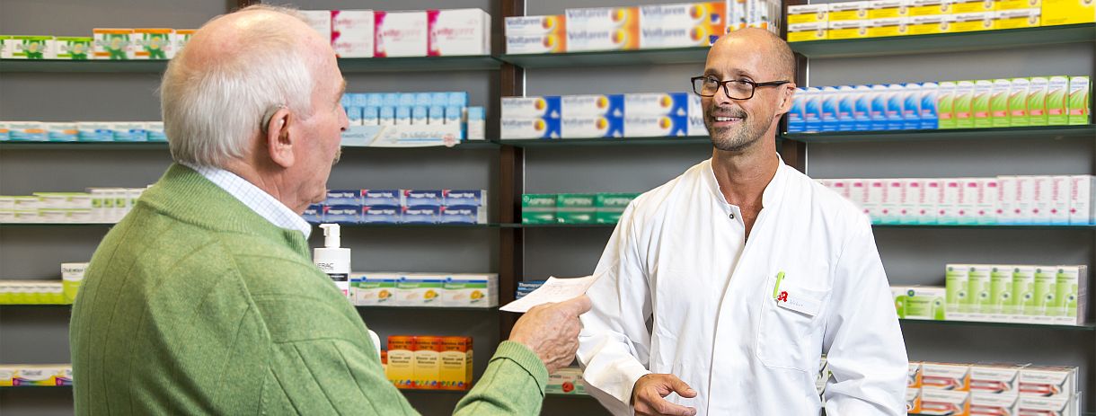 Ein Senior übergibt in einer Apotheke dem Apotheker ein Rezept