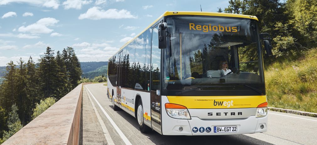 Gelber Linienbus befindet sich auf einer Straße unter Laubbäumen