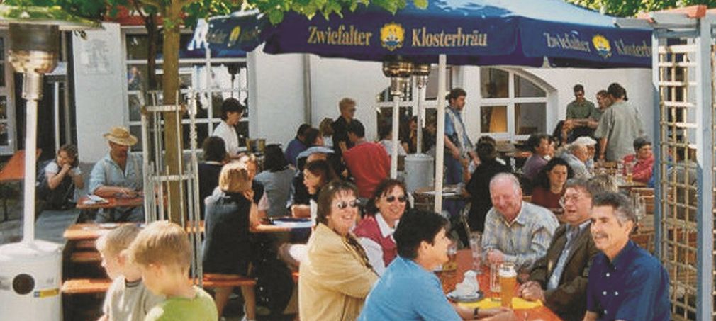 Personen an Biertischgarnitur unter einem Sonnenschirm