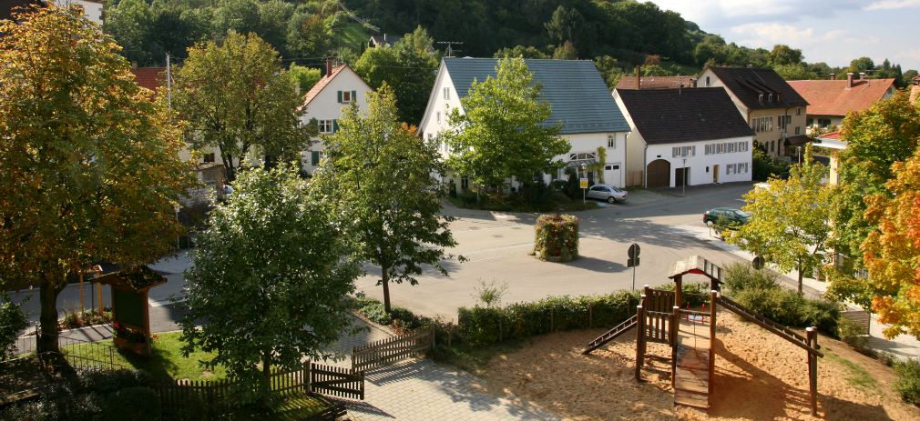 Titelbild des Flyers Unser Dorf hat Zukunft Häuser und Spielplatz mit Bäumen umgeben